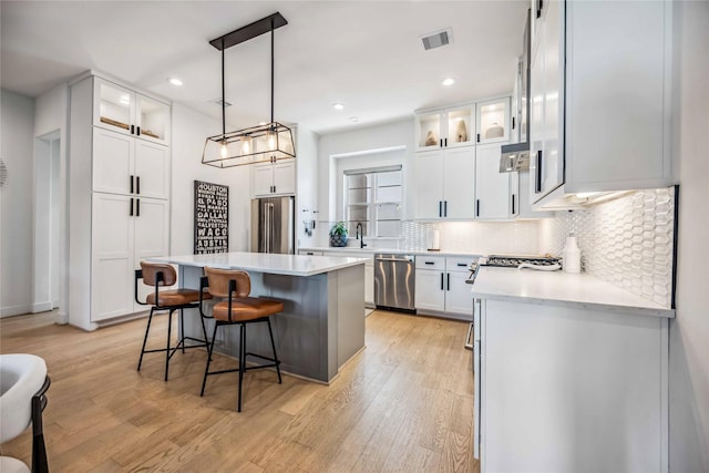 kitchen with a kitchen island, pendant lighting, white cabinets, stainless steel appliances, and light wood-type flooring