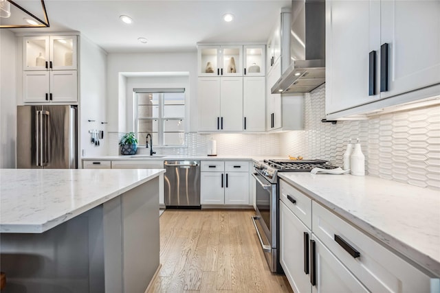 kitchen featuring stainless steel appliances, white cabinets, light stone counters, and wall chimney exhaust hood