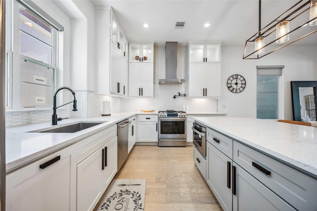 kitchen featuring light stone counters, white cabinets, appliances with stainless steel finishes, and wall chimney range hood