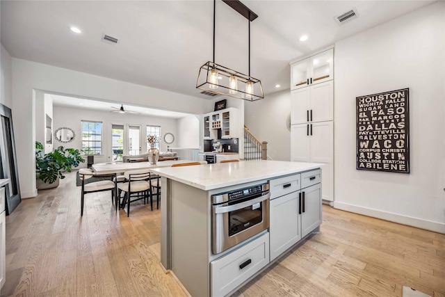 kitchen with ceiling fan, hanging light fixtures, light stone countertops, a kitchen island, and stainless steel oven