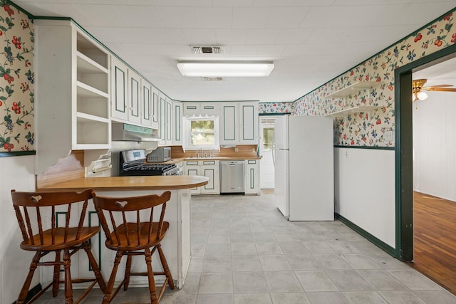 kitchen with kitchen peninsula, stove, stainless steel dishwasher, white fridge, and butcher block counters