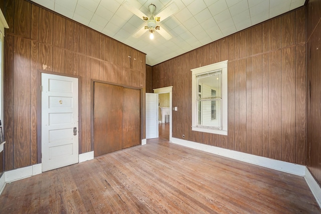 unfurnished bedroom with ceiling fan, wooden walls, and hardwood / wood-style flooring