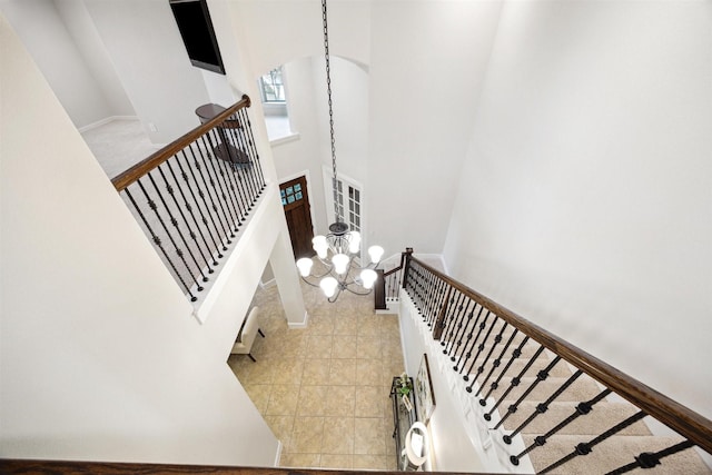 stairs with tile patterned floors, a towering ceiling, and an inviting chandelier