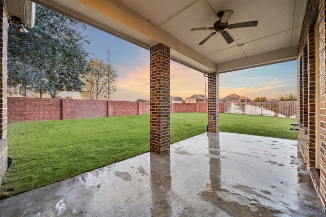 patio terrace at dusk featuring ceiling fan and a yard