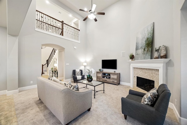 carpeted living room featuring a high ceiling, a stone fireplace, and ceiling fan