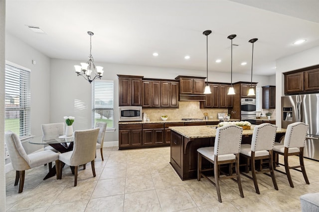 kitchen featuring pendant lighting, backsplash, a center island with sink, a notable chandelier, and stainless steel appliances