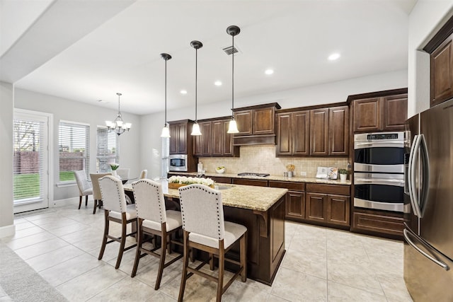 kitchen with pendant lighting, a center island with sink, a kitchen breakfast bar, light stone counters, and stainless steel appliances