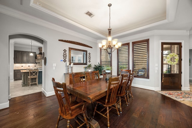 dining space featuring dark hardwood / wood-style flooring, crown molding, a raised ceiling, and a chandelier