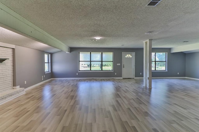 unfurnished living room featuring a brick fireplace, beamed ceiling, and light wood-type flooring