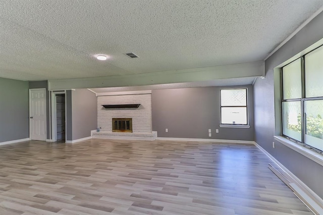 unfurnished living room with light wood-type flooring, a textured ceiling, and a brick fireplace