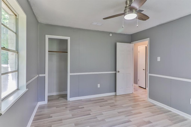 unfurnished bedroom featuring ceiling fan, a closet, light hardwood / wood-style flooring, and multiple windows