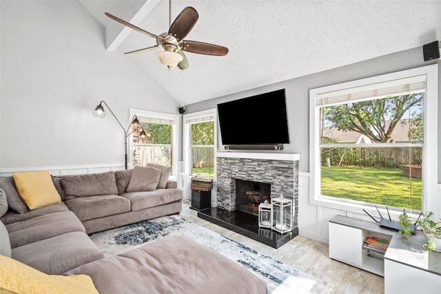 living room with lofted ceiling with beams, ceiling fan, a fireplace, a textured ceiling, and light hardwood / wood-style floors