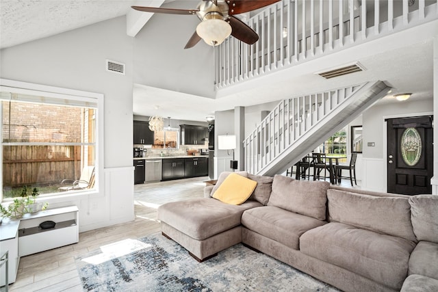 living room featuring ceiling fan, sink, high vaulted ceiling, and a textured ceiling