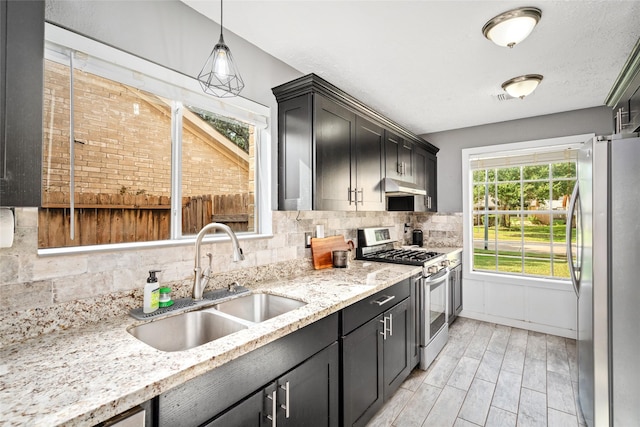 kitchen with sink, hanging light fixtures, tasteful backsplash, light stone counters, and appliances with stainless steel finishes