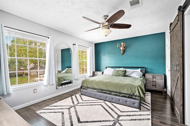 bedroom featuring dark hardwood / wood-style flooring, a barn door, a textured ceiling, and ceiling fan