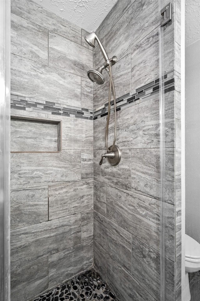 bathroom with tiled shower, a textured ceiling, and toilet