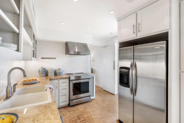 kitchen featuring light parquet flooring, stainless steel appliances, sink, white cabinetry, and wall chimney range hood