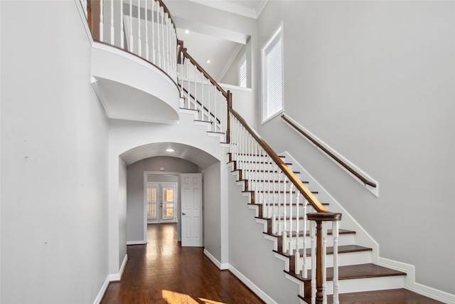 stairway featuring wood-type flooring, crown molding, and a high ceiling