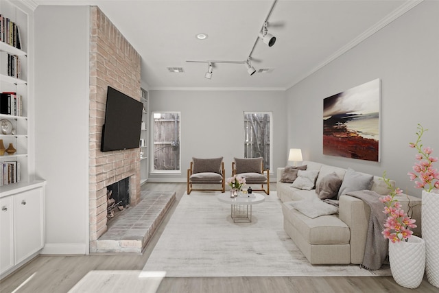 living room featuring visible vents, rail lighting, crown molding, light wood-type flooring, and a brick fireplace