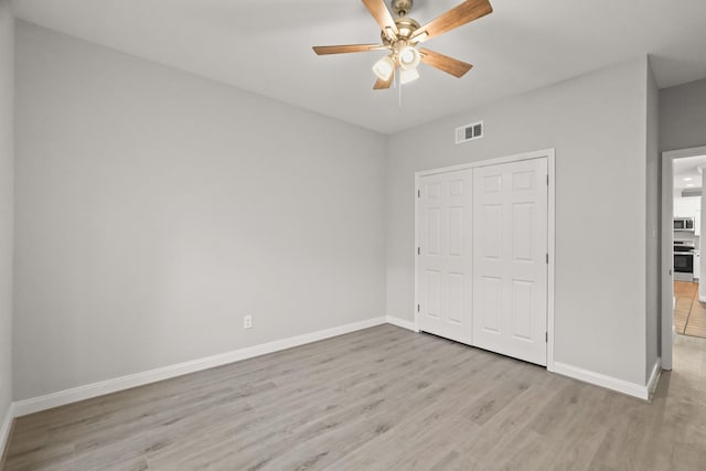 unfurnished bedroom featuring light wood finished floors, a closet, visible vents, ceiling fan, and baseboards