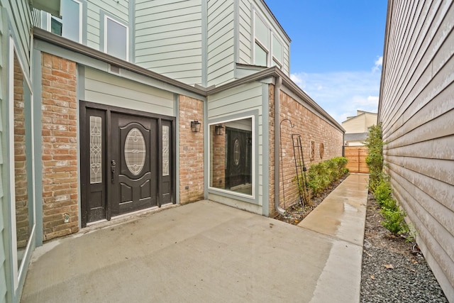 view of exterior entry with a patio, brick siding, and fence