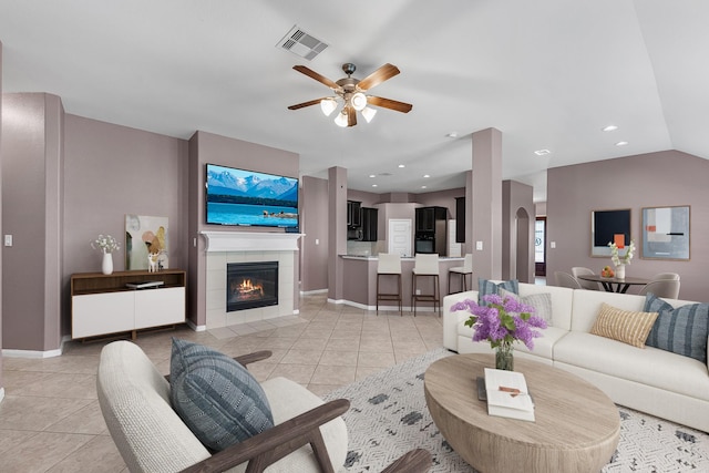 tiled living room with ceiling fan, lofted ceiling, and a tiled fireplace