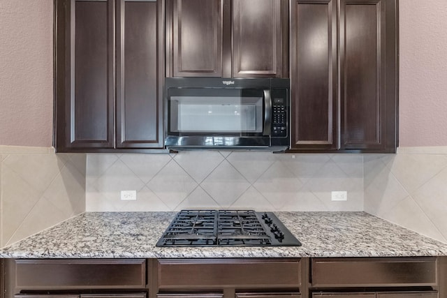 kitchen with dark brown cabinets, tasteful backsplash, light stone counters, and black appliances