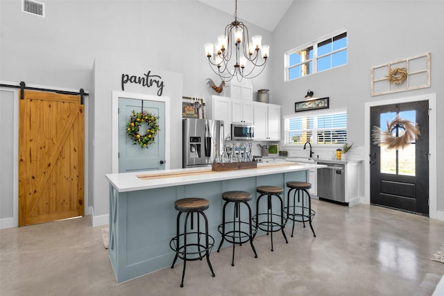 kitchen featuring white cabinetry, a center island, a barn door, decorative light fixtures, and appliances with stainless steel finishes