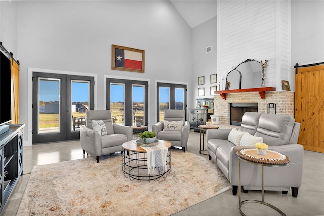 living room with a barn door, french doors, high vaulted ceiling, and a brick fireplace