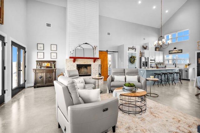 living room with sink, a brick fireplace, an inviting chandelier, a barn door, and high vaulted ceiling