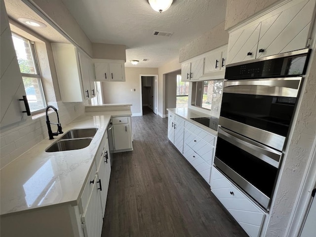 kitchen featuring white cabinetry, sink, stainless steel double oven, and plenty of natural light