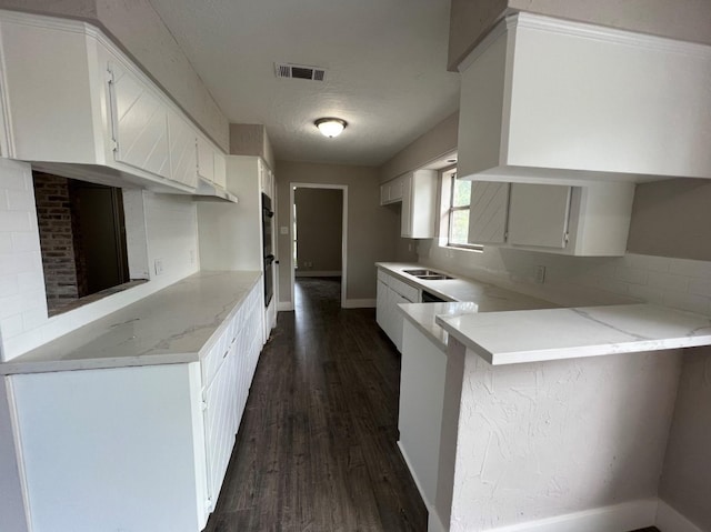 kitchen with kitchen peninsula, a textured ceiling, dark wood-type flooring, sink, and white cabinetry