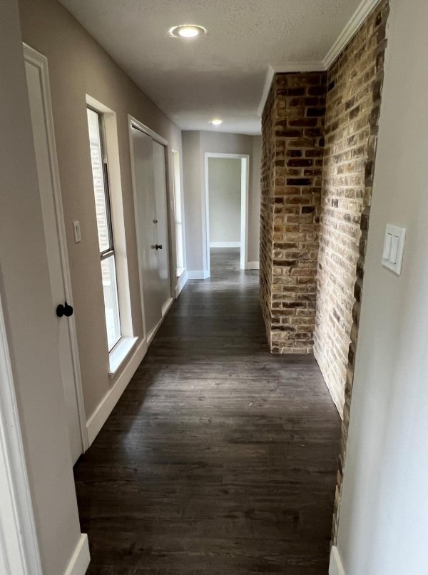 corridor with a textured ceiling, dark hardwood / wood-style floors, and ornamental molding