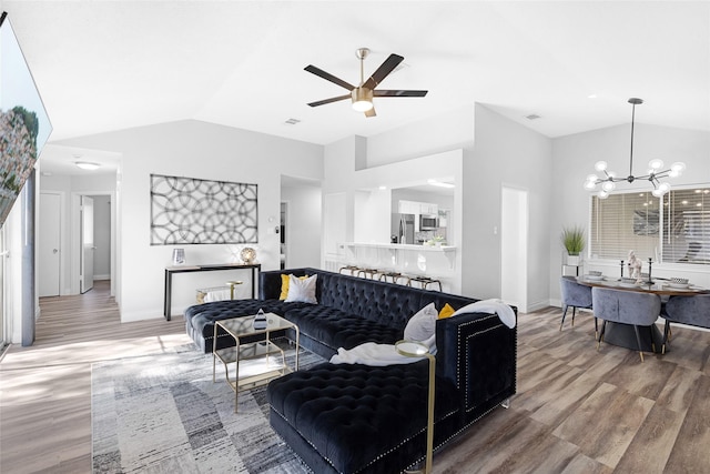 living room with ceiling fan with notable chandelier, wood-type flooring, and vaulted ceiling