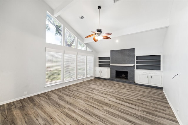 unfurnished living room with a brick fireplace, built in shelves, ceiling fan, beam ceiling, and hardwood / wood-style floors