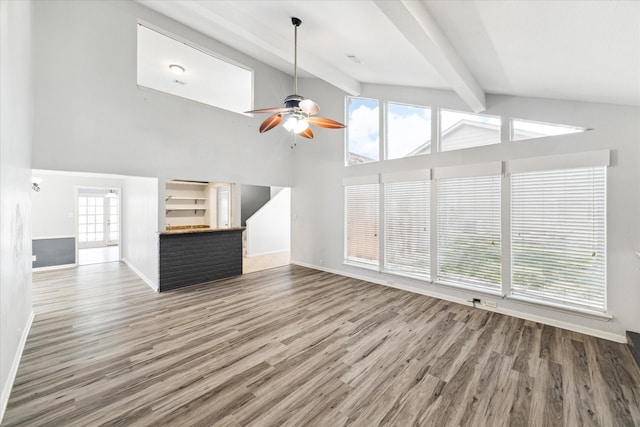 unfurnished living room with vaulted ceiling with beams, a wealth of natural light, ceiling fan, and wood-type flooring