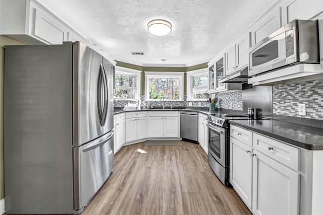 kitchen with crown molding, appliances with stainless steel finishes, white cabinets, tasteful backsplash, and light hardwood / wood-style floors