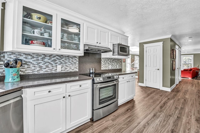 kitchen with appliances with stainless steel finishes, white cabinets, backsplash, a textured ceiling, and ornamental molding