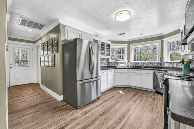 kitchen featuring ornamental molding, light wood-type flooring, white cabinetry, and stainless steel appliances