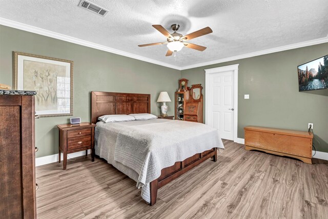 bedroom with light wood-type flooring, a textured ceiling, ceiling fan, and ornamental molding