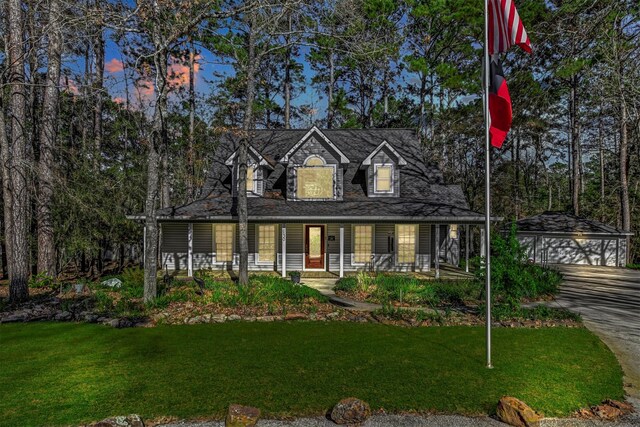 cape cod house with covered porch, a lawn, an outbuilding, and a garage