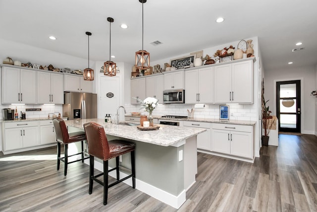 kitchen featuring sink, an island with sink, appliances with stainless steel finishes, decorative light fixtures, and white cabinetry