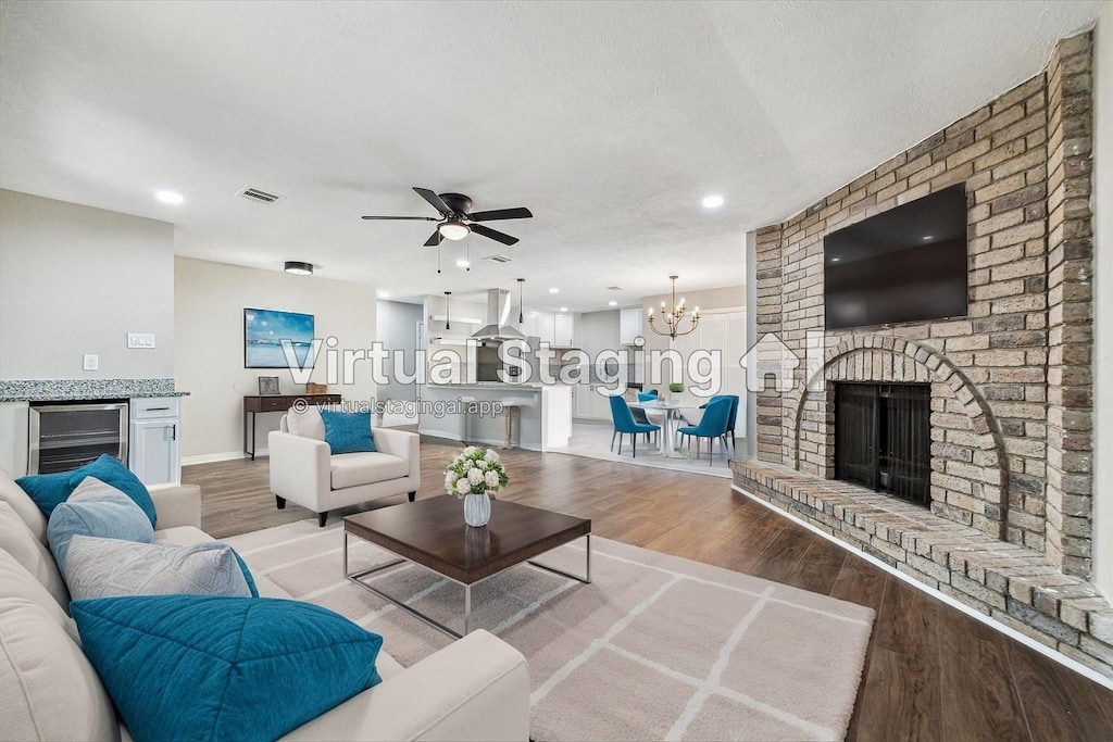 living room with beverage cooler, a brick fireplace, light hardwood / wood-style flooring, a textured ceiling, and ceiling fan with notable chandelier