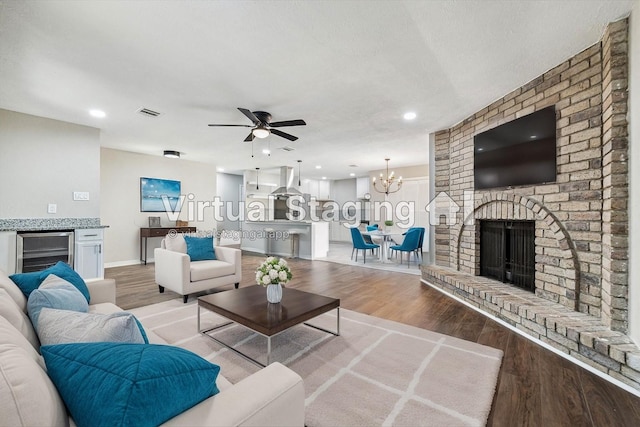 living room with beverage cooler, a brick fireplace, light hardwood / wood-style flooring, a textured ceiling, and ceiling fan with notable chandelier