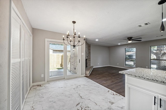 interior space with light stone countertops, hanging light fixtures, a fireplace, white cabinets, and ceiling fan with notable chandelier