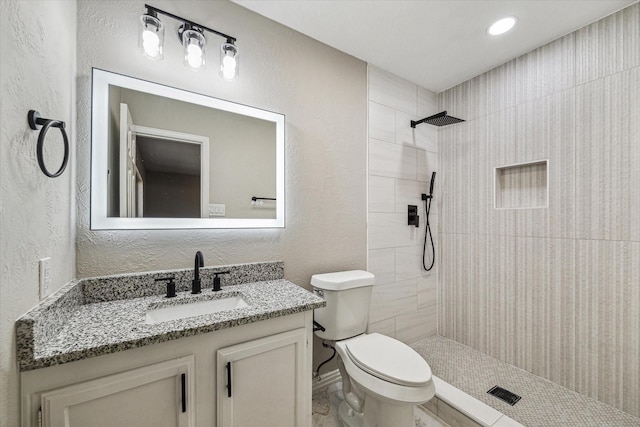 bathroom featuring a tile shower, vanity, and toilet