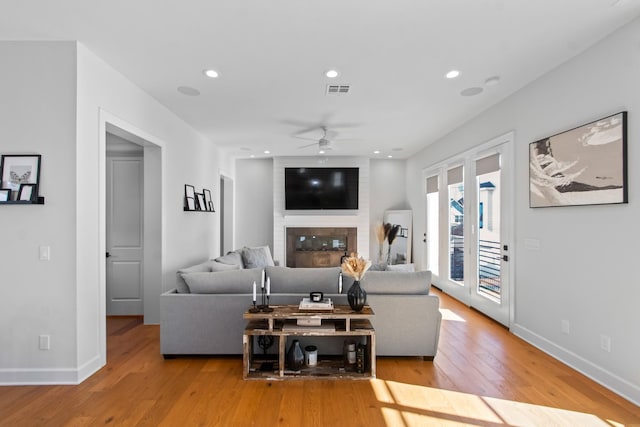 living room with ceiling fan, a fireplace, and light hardwood / wood-style flooring