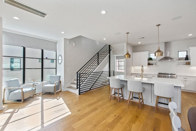 kitchen with sink, an island with sink, white cabinets, decorative light fixtures, and wall chimney exhaust hood