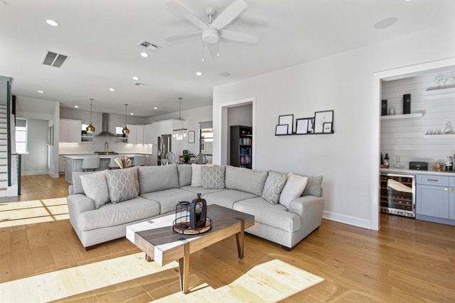 living room featuring ceiling fan, beverage cooler, indoor wet bar, and light wood-type flooring