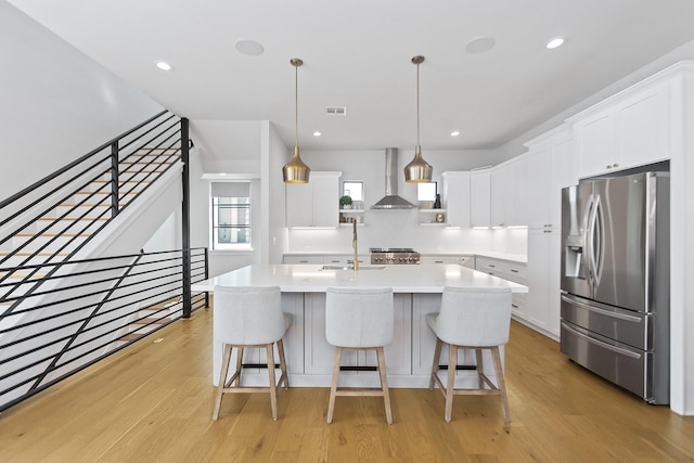 kitchen featuring pendant lighting, stainless steel fridge with ice dispenser, wall chimney range hood, and white cabinets